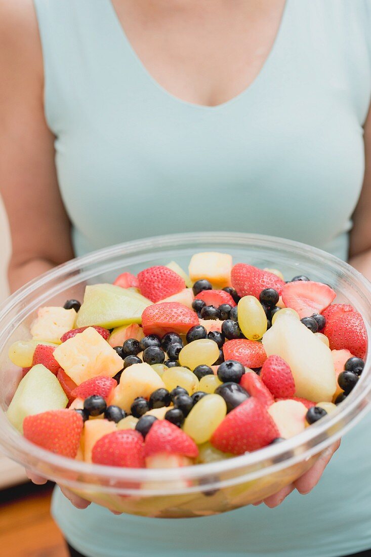 Frau hält grosse Plastikschale mit Obstsalat