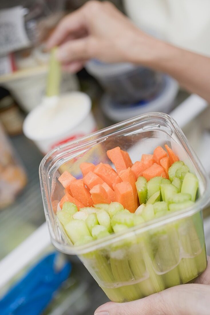 Woman dipping celery in yoghurt in refrigerator