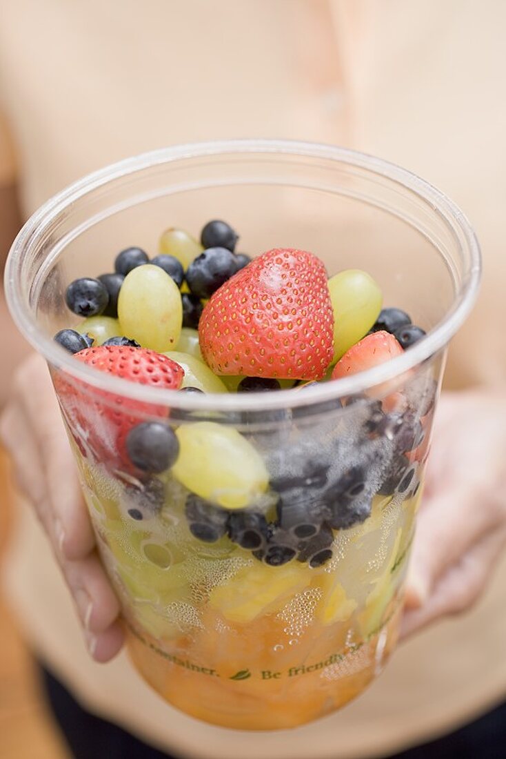 Frau hält Plastikbecher mit Obstsalat