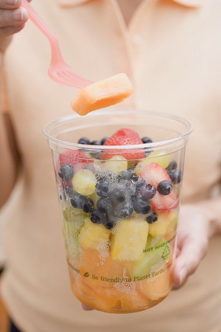Woman taking piece of melon out of plastic tub of fruit salad