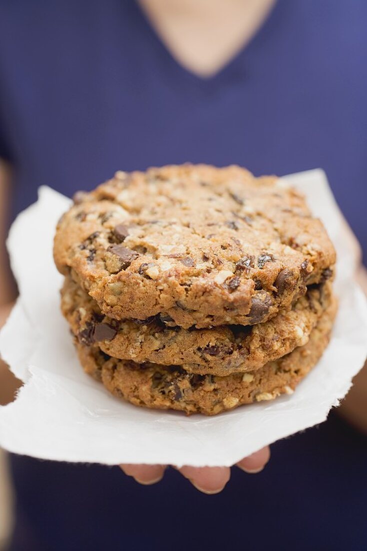 Frau hält grosse Chocolate Chip Cookies auf Papier