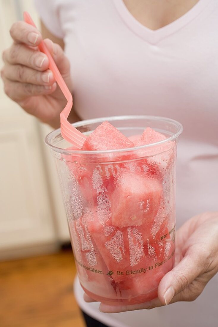 Frau isst Melonenwürfel aus Plastikbecher