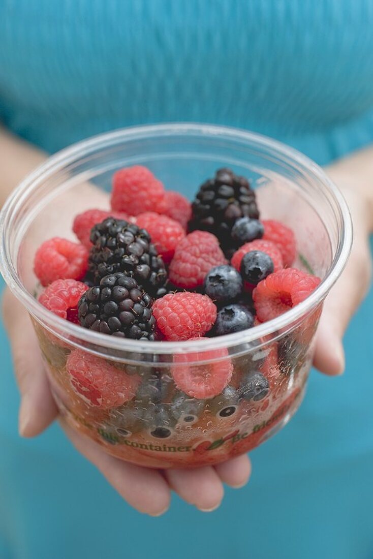 Woman holding plastic tub of fresh berries