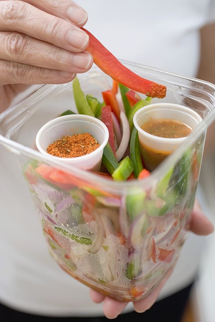 Woman holding plastic container of vegetables, seasonings & dip