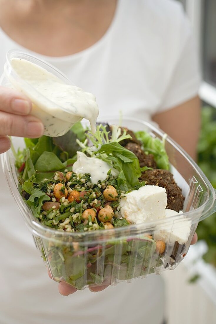 Frau giesst Dressing über Salat in Plastikschale