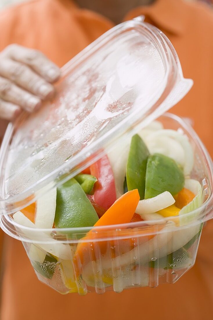 Frau hält Plastikschale mit Gemüse