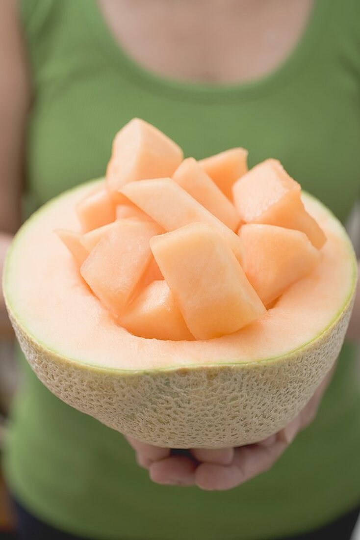 Frau hält Melonenwürfel in ausgehöhlter Cantaloupemelone