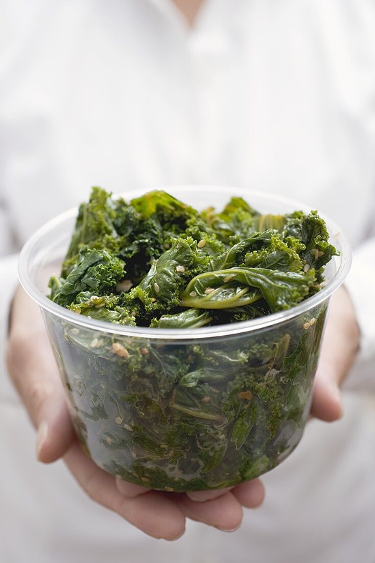 Woman holding plastic tub of cooked kale