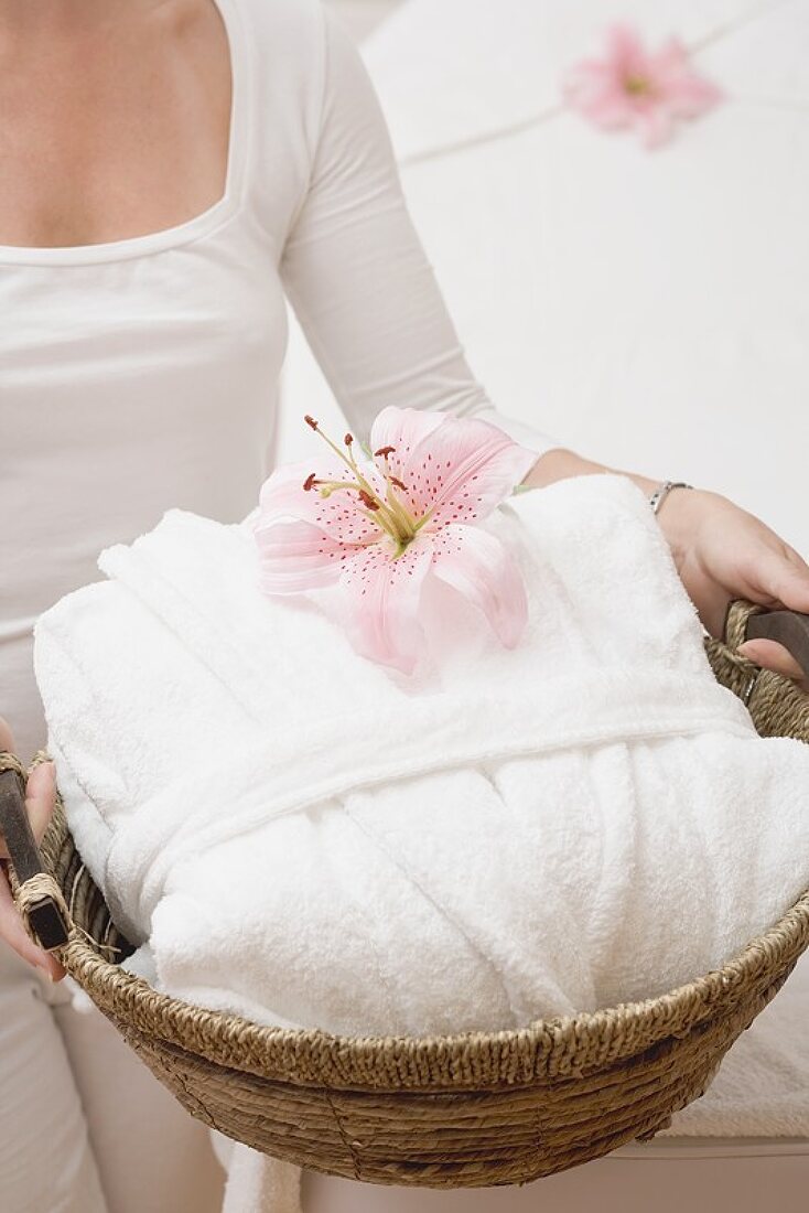 Woman holding white bathrobe and orchid in basket