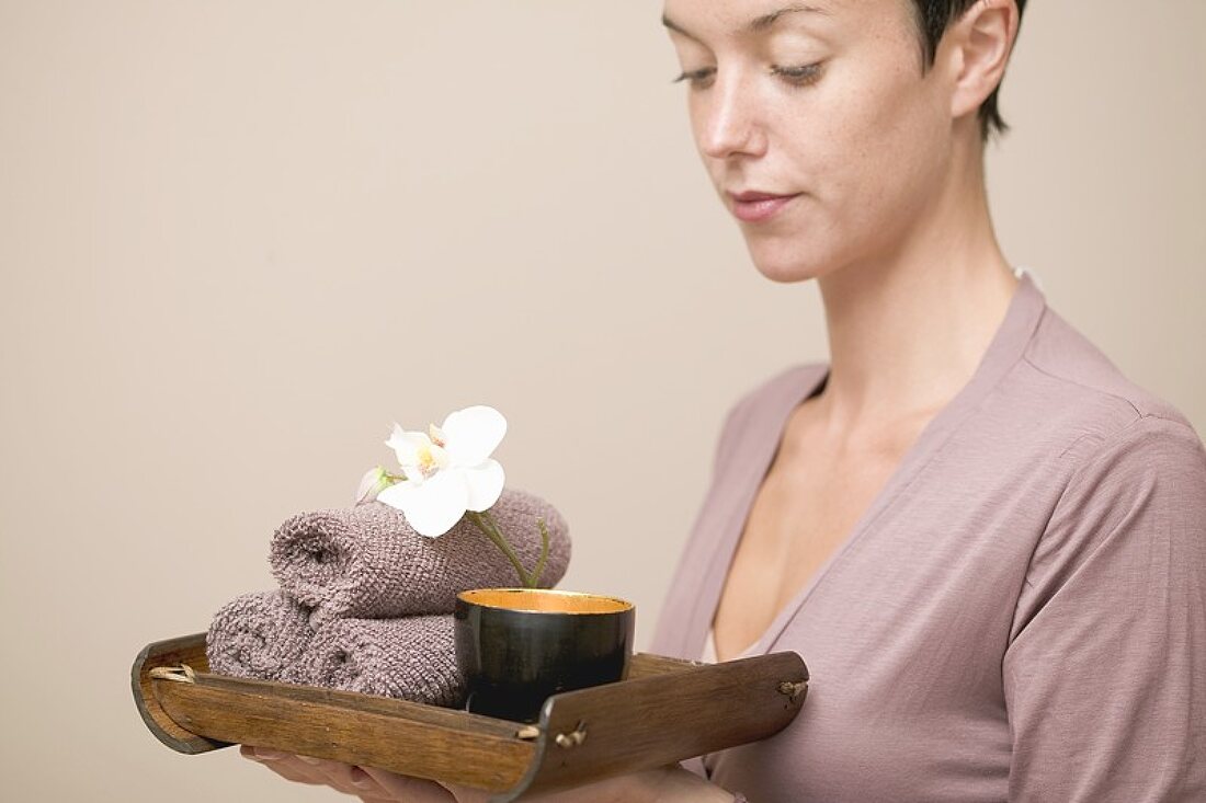 Frau hält Tablett mit Wasserschale, Orchidee und Handtüchern