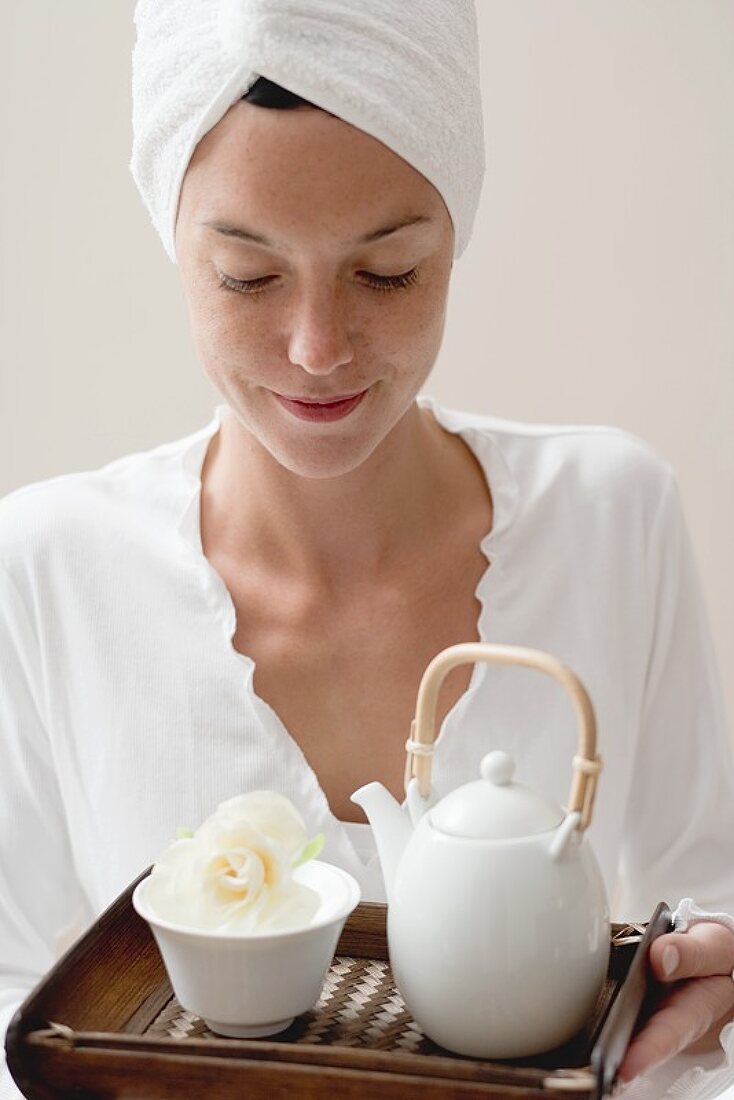 Frau hält Tablett mit Tee und weisser Blüte