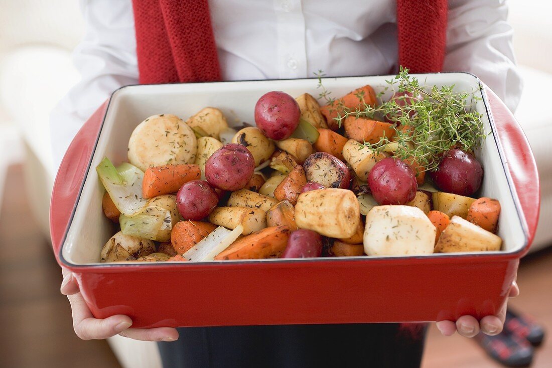 Woman holding roasting dish full of roasted root vegetables