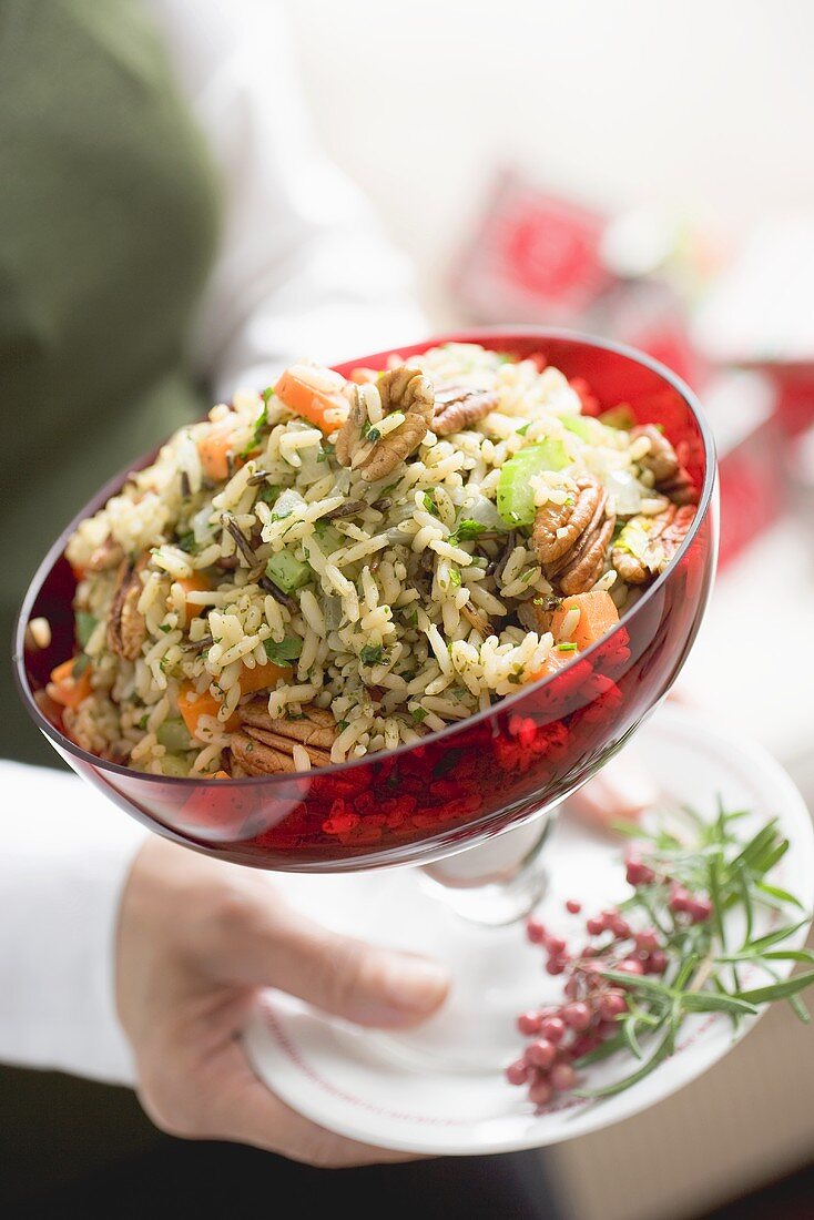 Woman holding bowl of vegetable rice with pecans (Christmas)