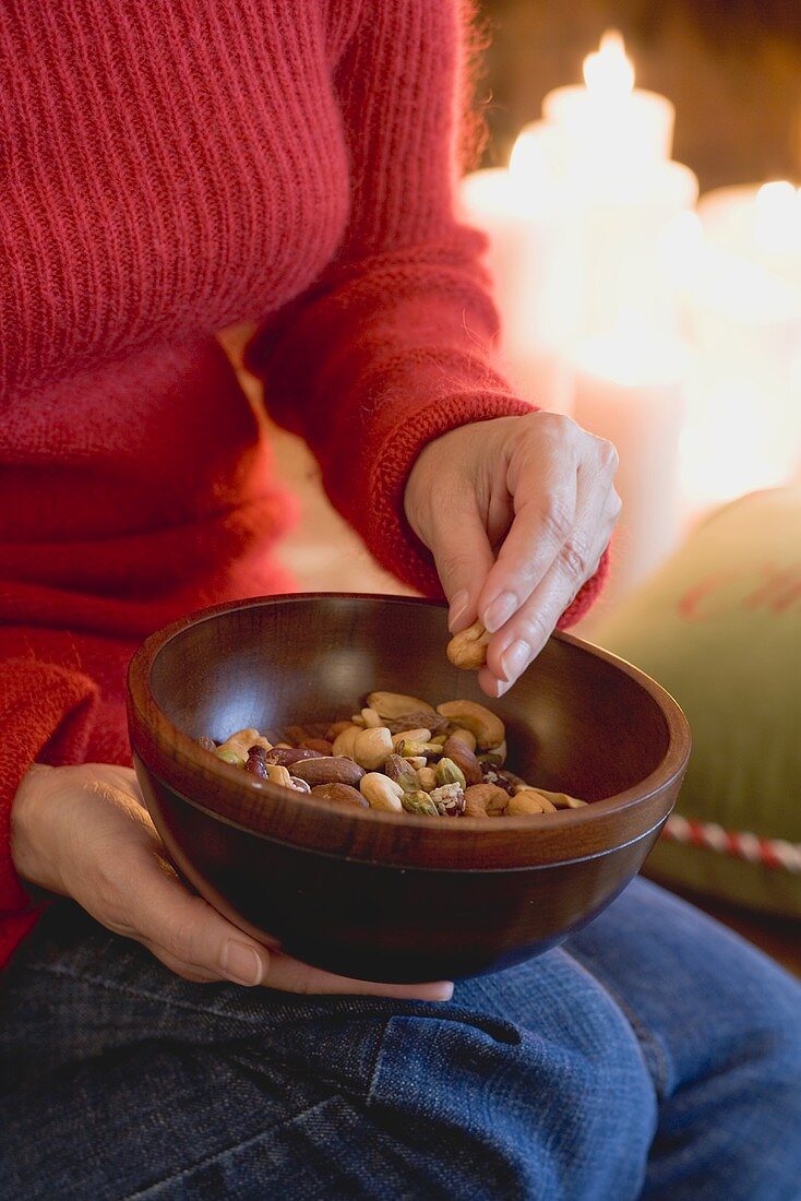 Woman eating nuts out of wooden bowl (Christmas)