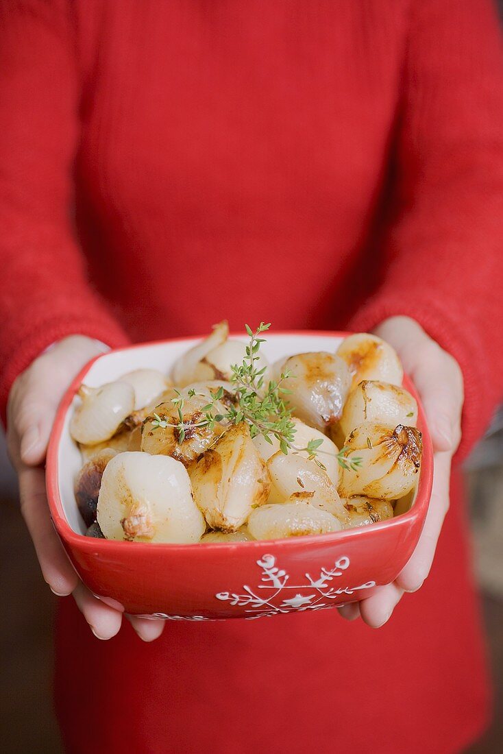 Woman holding dish of roasted onions (Christmas)