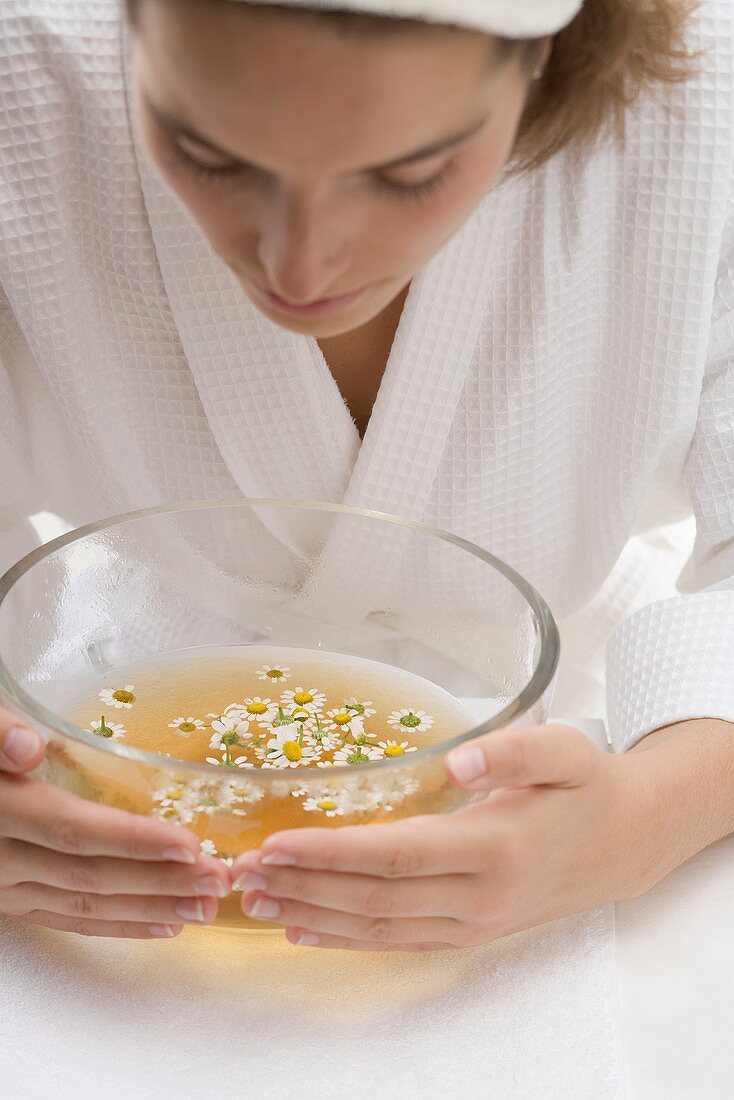 Woman bending over bowl of chamomile tea with flowers