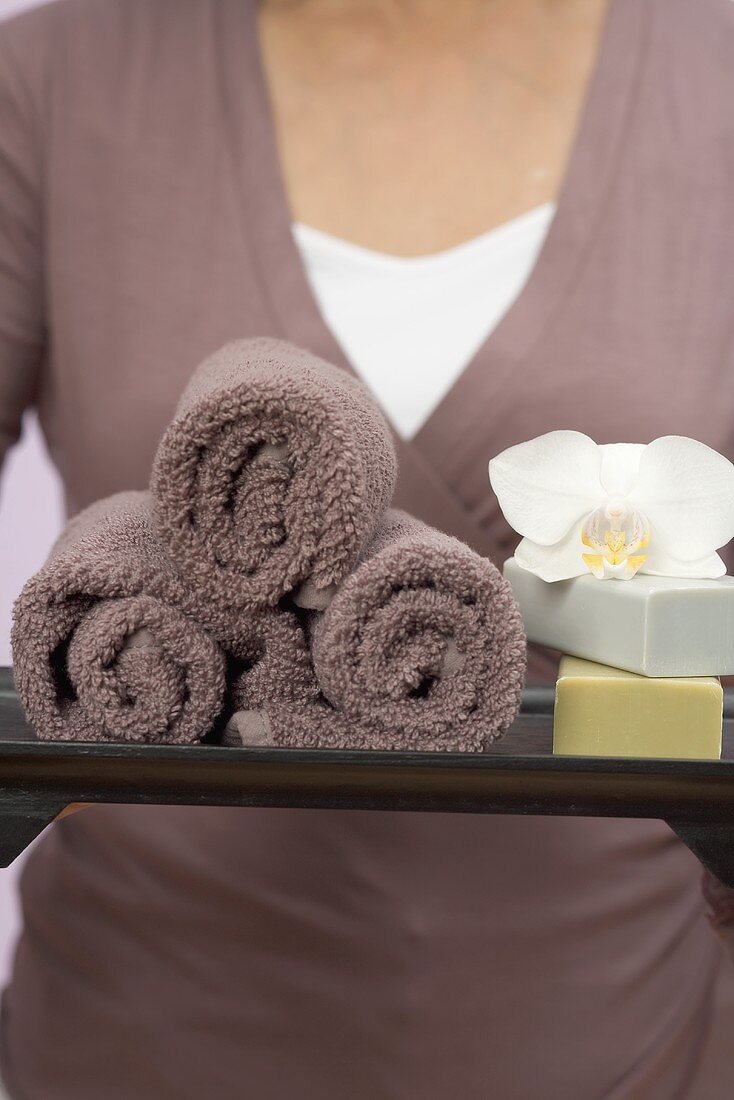 Frau hält Tablett mit Handtüchern, Seifen und Orchidee