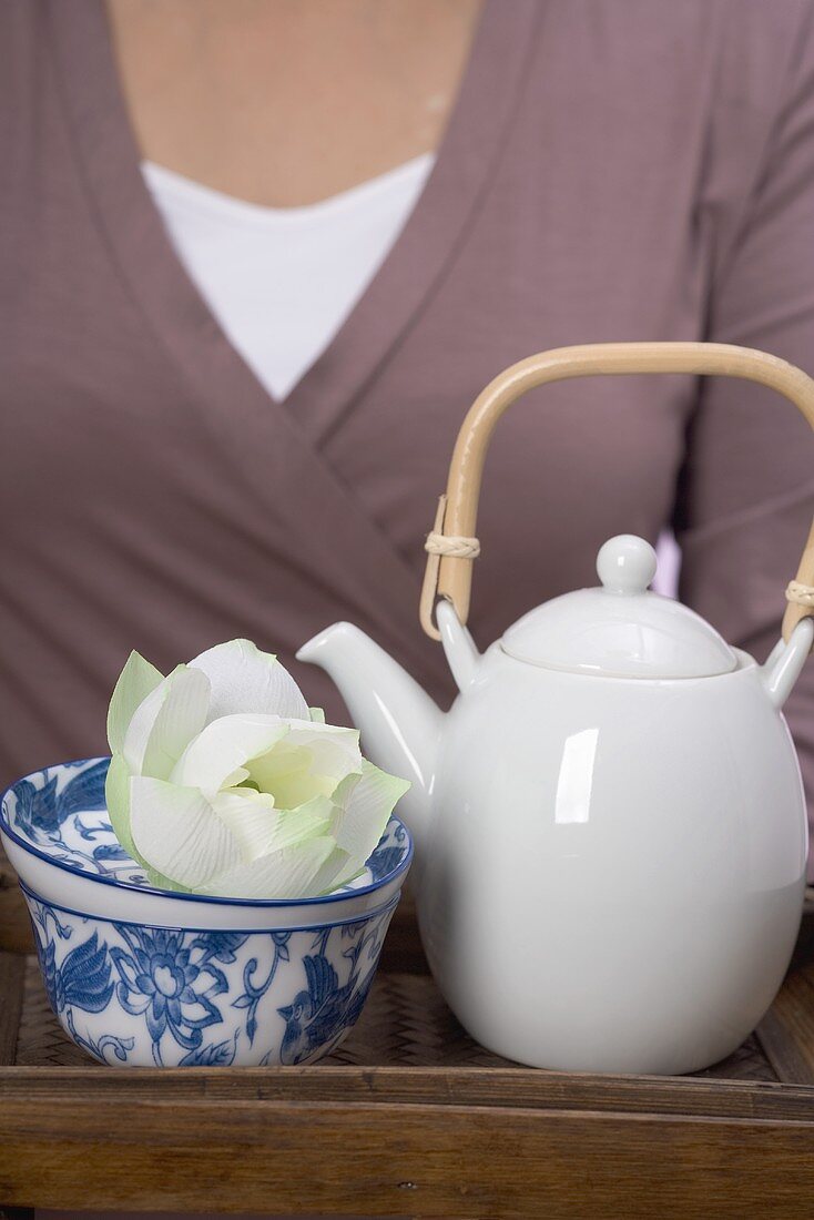 Woman holding teapot, tea bowl and flower on tray