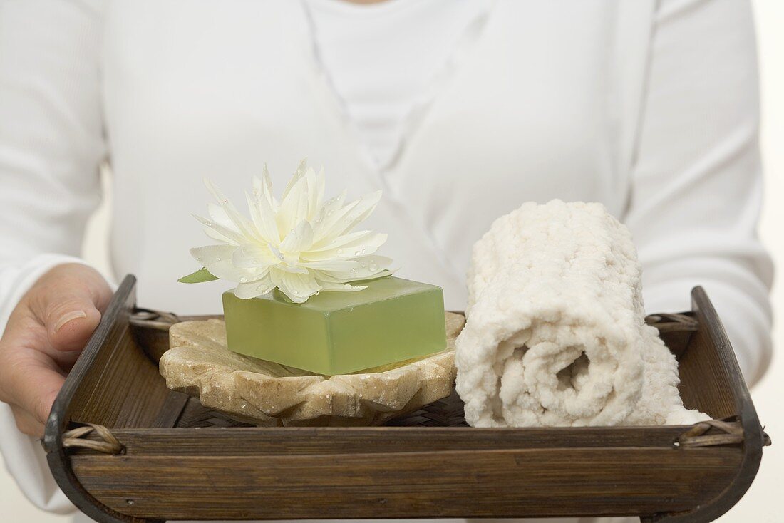 Woman holding soap, water lily and towel on tray