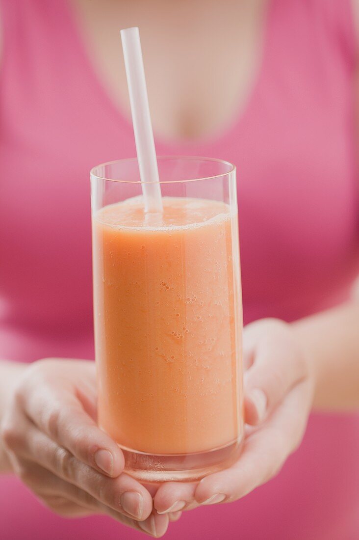 Woman holding glass of mango smoothie with straw