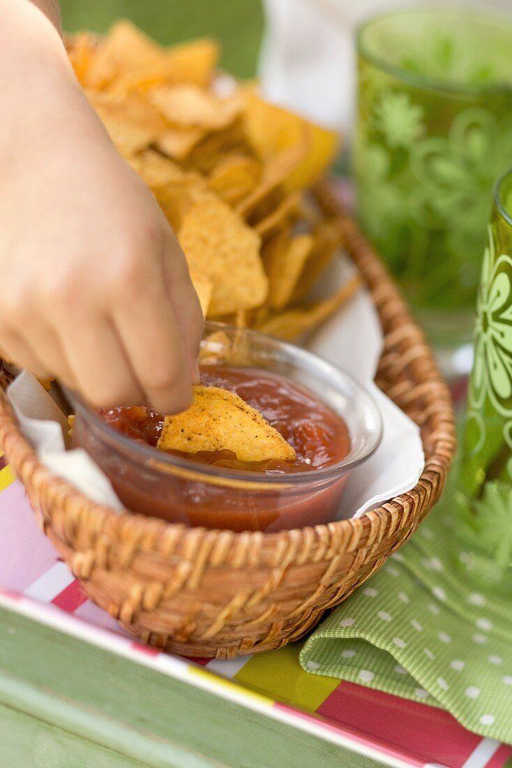Child's hand dipping tortilla chip in salsa