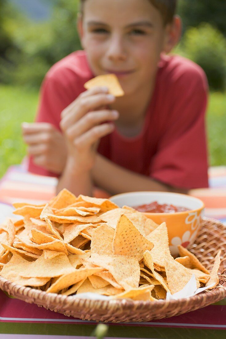 Junge isst Nachos mit Salsa im Garten