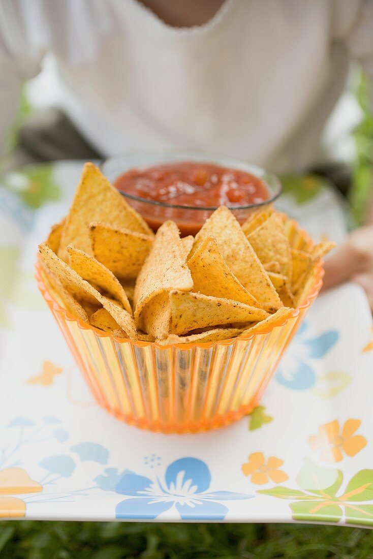 Child holding nachos and tomato salsa on tray