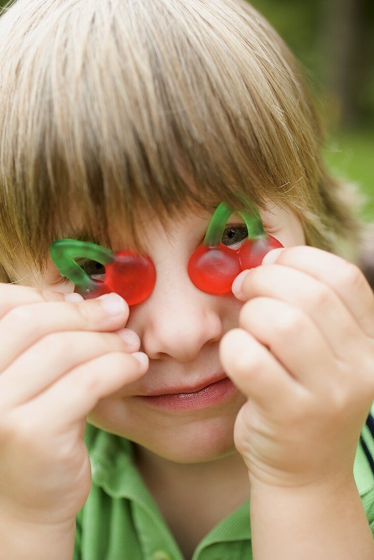 Kleiner Junge hält Kirschen aus Fruchtgummi vor seine Augen
