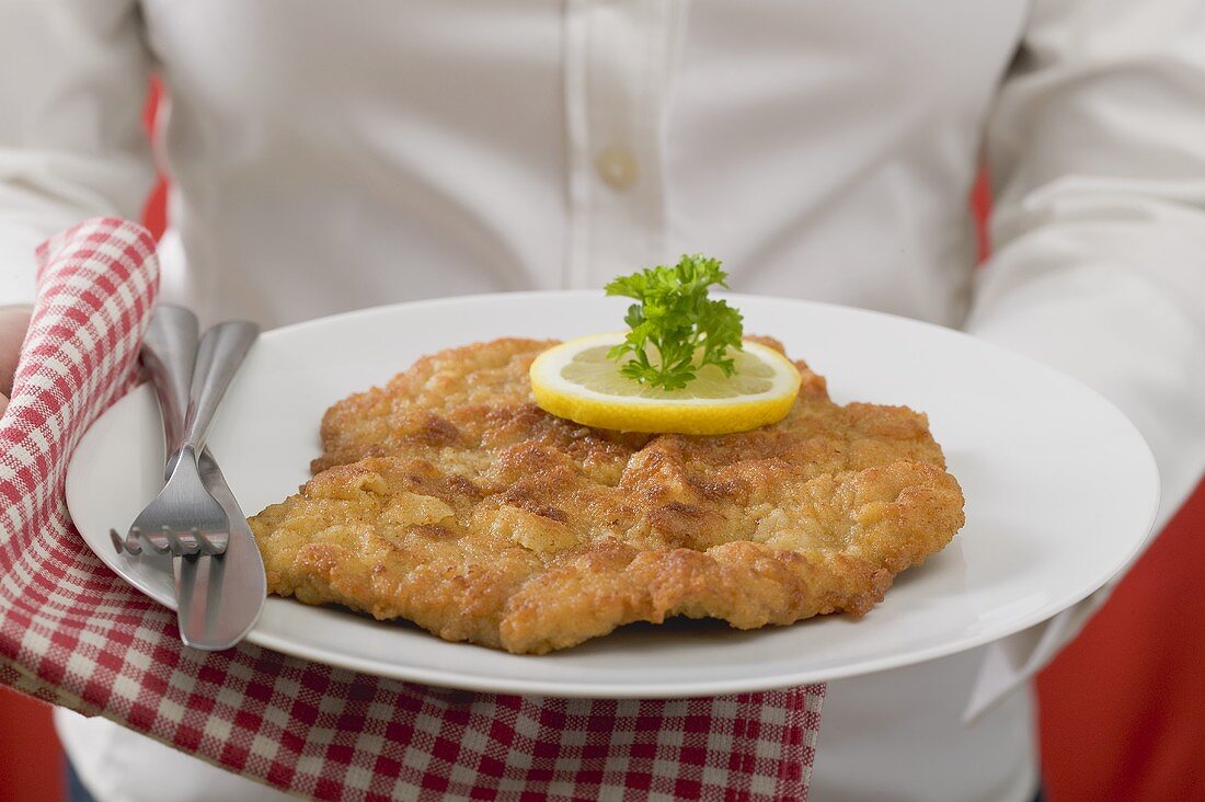 Woman holding plate of Wiener schnitzel (veal escalope)