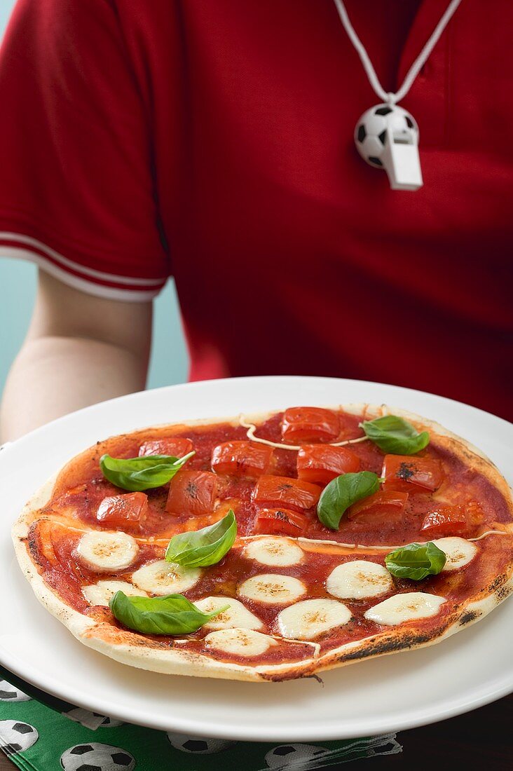Fussballspielerin hält Tomaten-Mozzarella-Pizza mit Basilikum