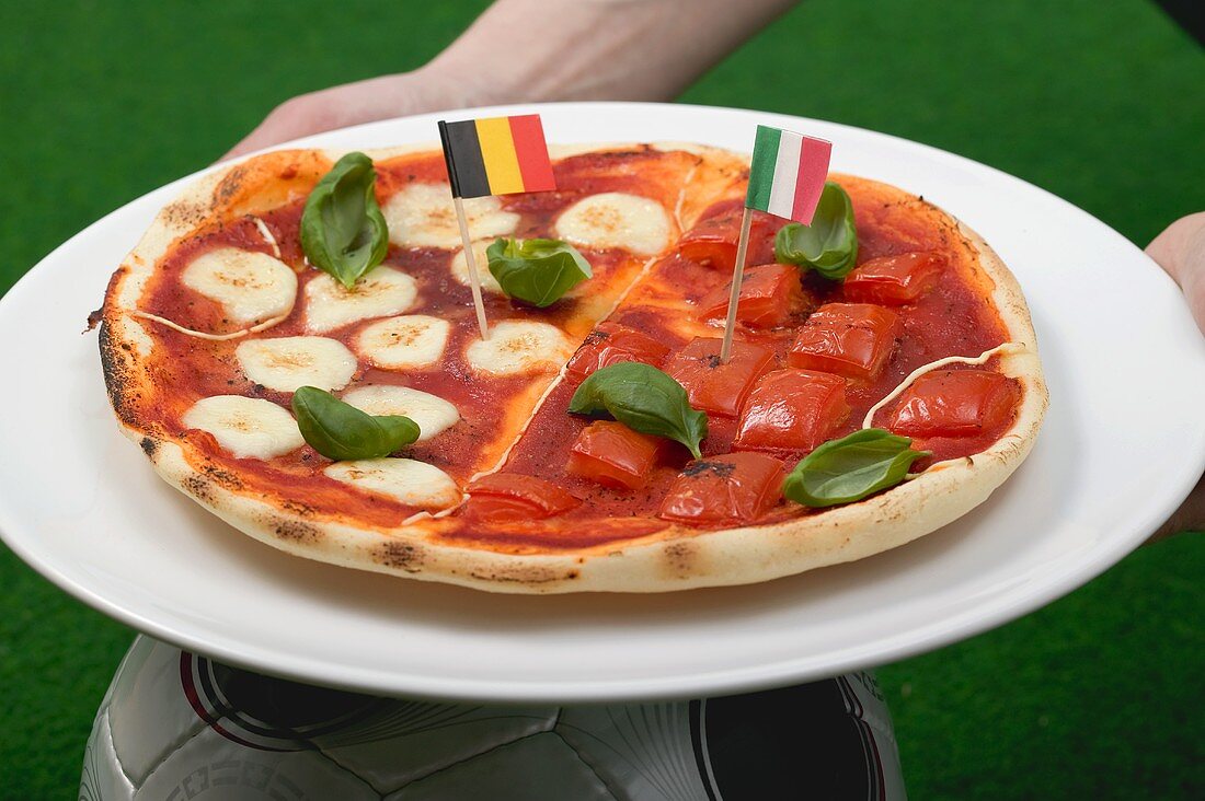 Hände halten Tomaten-Mozzarella-Pizza mit Flaggen