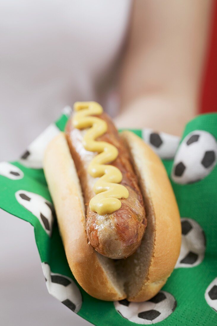 Woman holding hot dog with mustard on napkin with football motifs