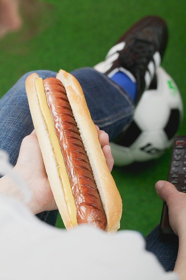 Fussballfan hält Hot Dog mit Senf und Fernbedienung
