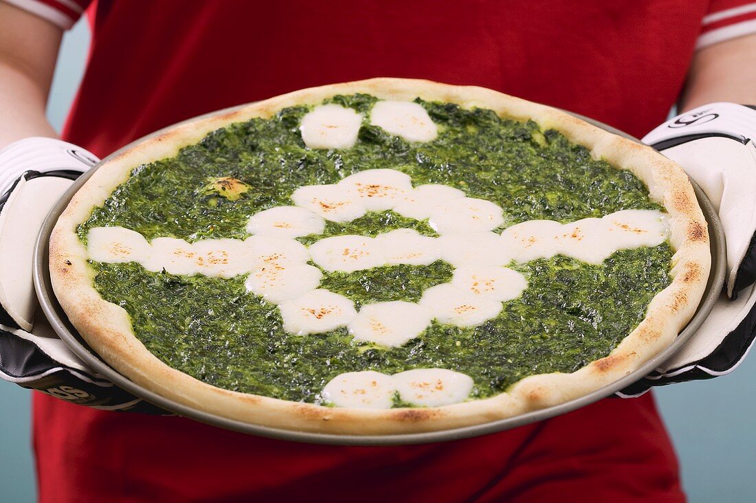 Female footballer holding spinach and mozzarella pizza