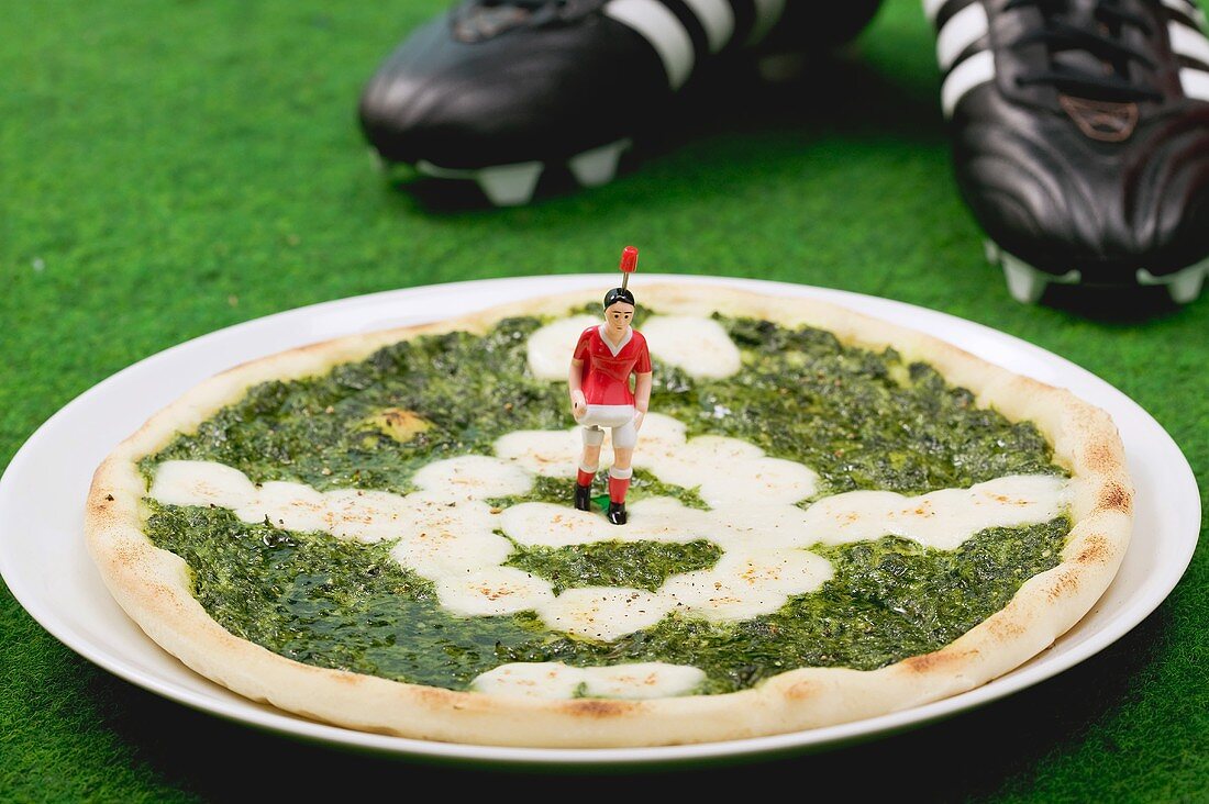 Spinatpizza mit Mozzarella, Fussballschuhe im Hintergrund