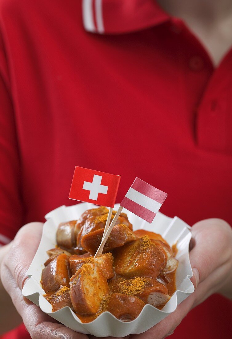 Woman holding currywurst with two flags in paper dish
