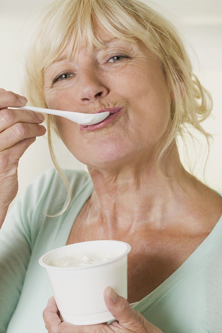 Frau isst Joghurt aus Plastikbecher
