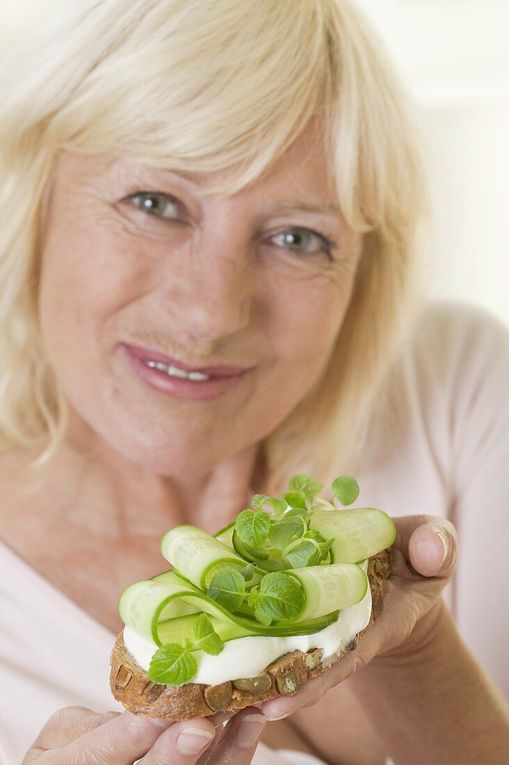 Woman holding slice of bread with yoghurt & cucumber slices