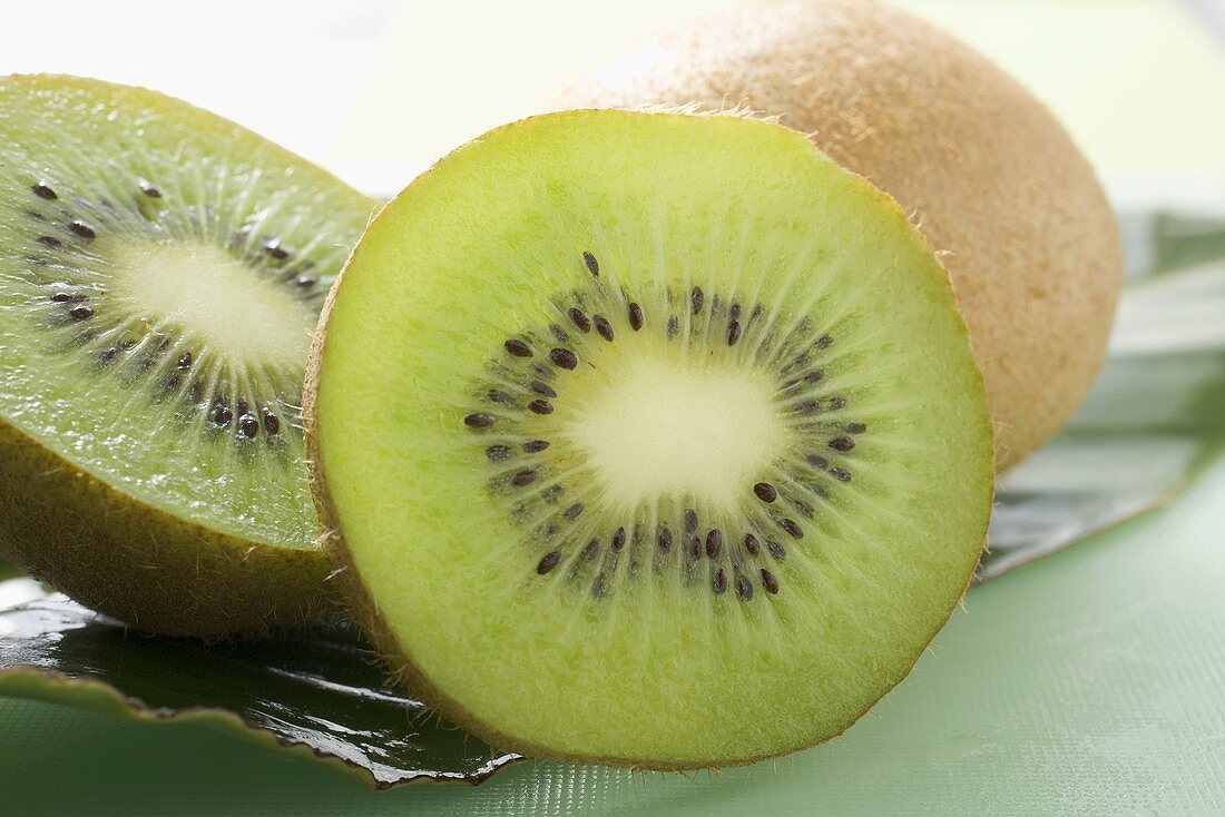Two halves of a kiwi fruit in front of whole kiwi fruit