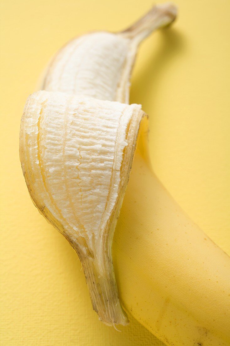 Banane, halb geschält, auf gelbem Untergrund