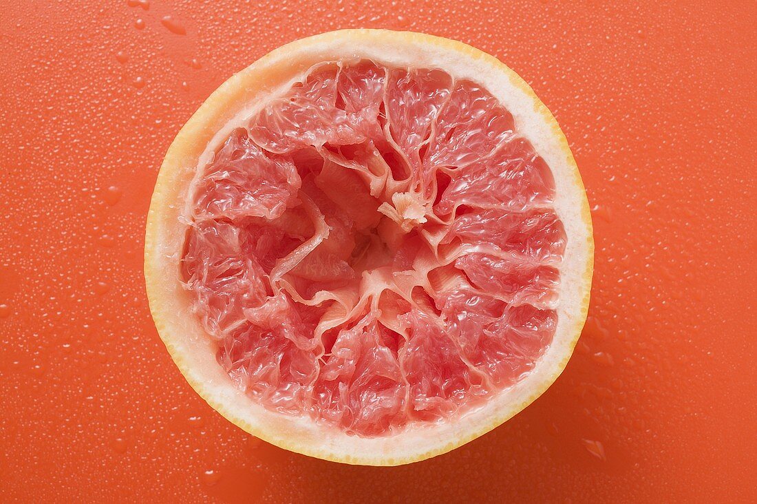 Ausgepresste rosa Grapefruit auf orangefarbenem Untergrund