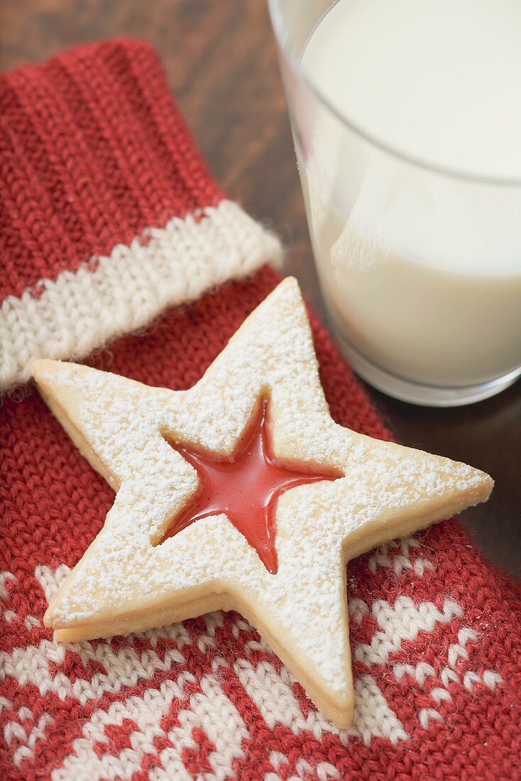 Jam-filled star biscuit on woollen mitten, glass of milk (Xmas)