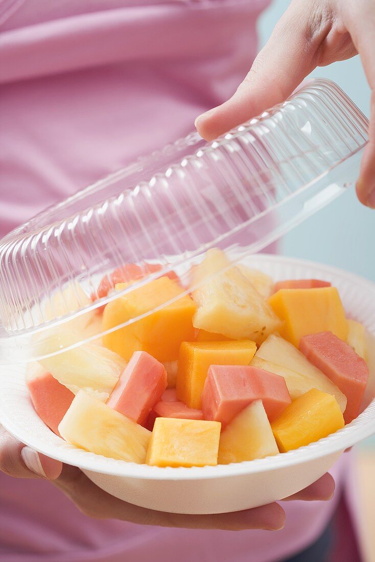 A woman removing a lid from plastic dish of exotic fruit salad