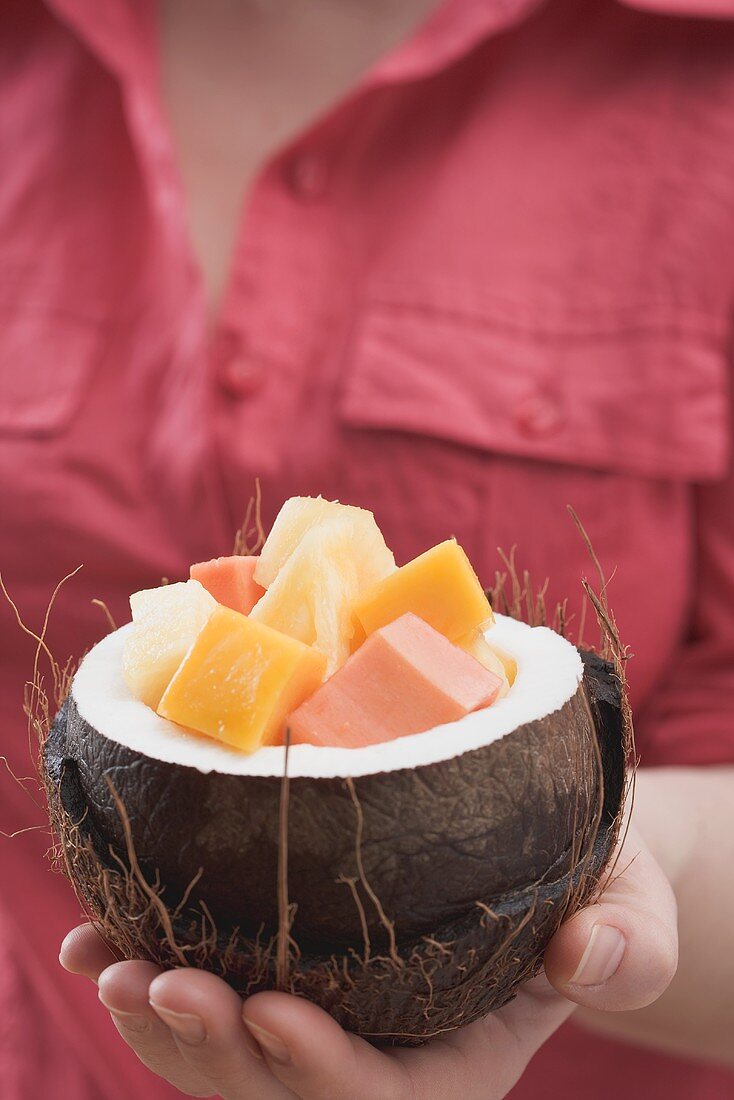 Frau hält ausgehöhlte Kokosnuss mit exotischem Fruchtsalat