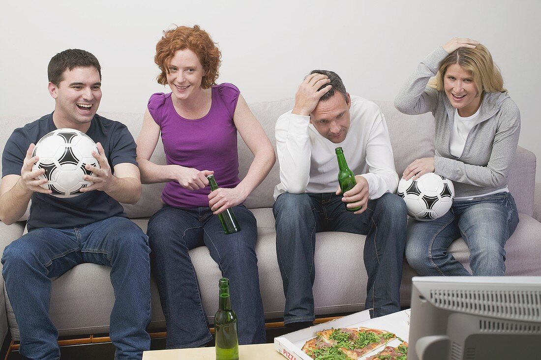 Friends in front of TV with footballs, beer and pizza