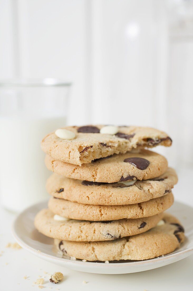 Chocolate chip cookies, one with a bite taken, & glass of milk