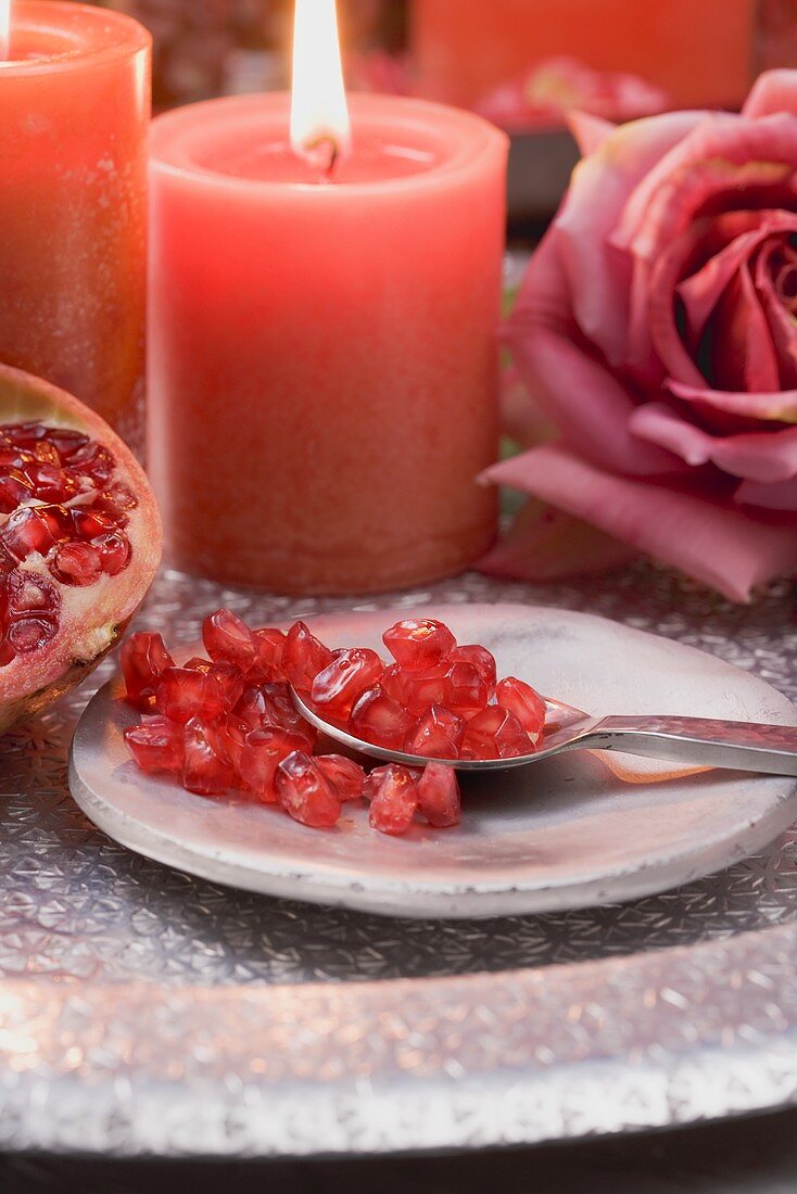Granatapfelkerne auf Teller mit Löffel, rote Kerzen und Rose