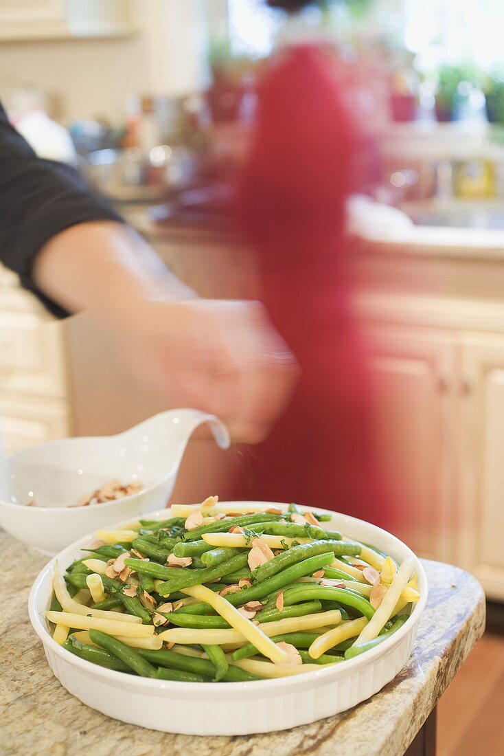 Hand scattering flaked almonds on beans, woman in background