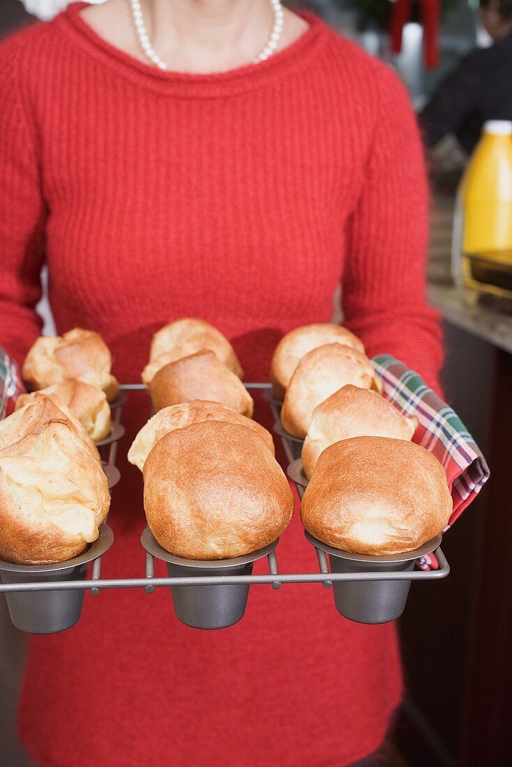 Woman holding freshly baked popovers on a rack