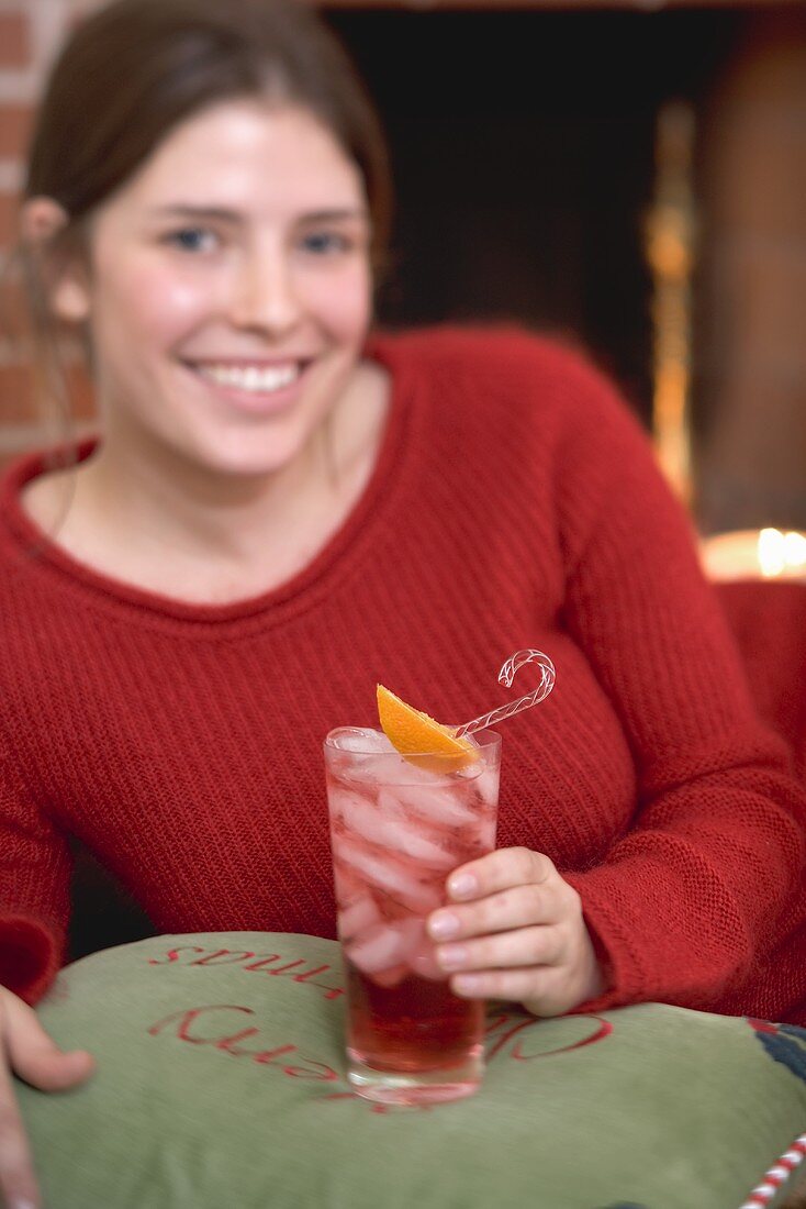 Woman holding glass of Campari with ice cubes in front of fireplace